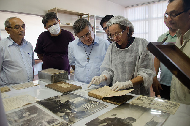 De luvas, touca e bata branca, Débora Mendes mostra para a comitiva de freis alguns dos documentos que serão preservados e conservados.